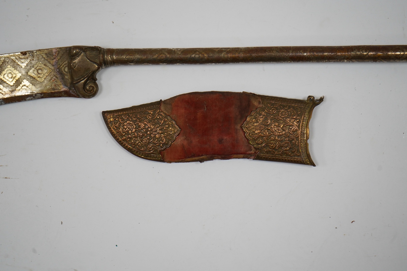 An Indian axe bhuj, with broad curved blade, iron haft with elephant head top, all covered over with silver gilt foil engraved with flower heads, the pommel unscrews to reveal a stiletto, with its copper mounted sheath,